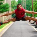 A young man in athletic wear performing a high jump outdoors in a parking area, showcasing fitness and agility.