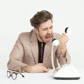 Businessman in a beige suit shouting into a vintage telephone, expressing frustration at work.