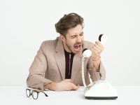 Businessman in a beige suit shouting into a vintage telephone, expressing frustration at work.