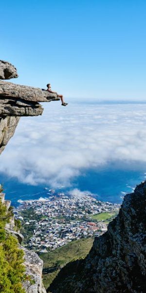 pexels-photo-1659438-1659438 A person sits on a cliff edge enjoying a breathtaking view of the ocean and city below.