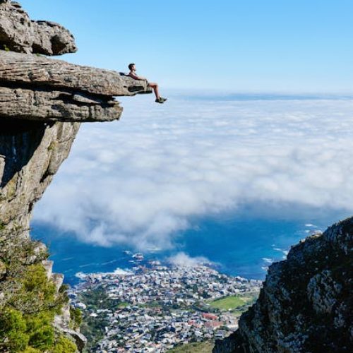 A person sits on a cliff edge enjoying a breathtaking view of the ocean and city below.