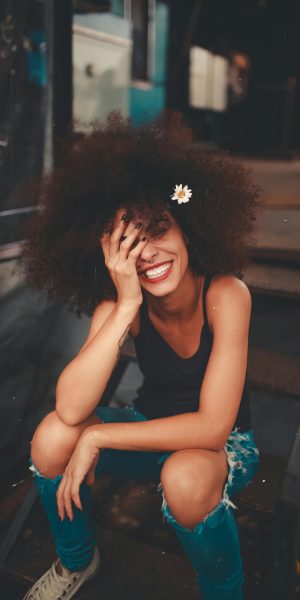 pexels-photo-1848565-1848565 Cheerful woman wearing ripped jeans and curly hair with flower, enjoying a sunny day outdoors.