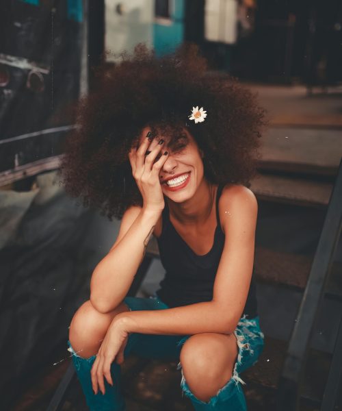Cheerful woman wearing ripped jeans and curly hair with flower, enjoying a sunny day outdoors.
