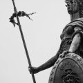 A monochrome photograph showcasing a classic statue holding a spear and shield, exuding timeless strength.