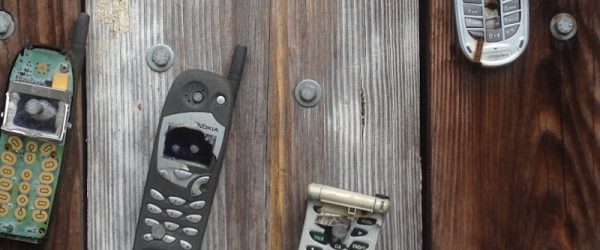 Collection of vintage cell phones attached to a rustic wooden wall with a humorous sign.