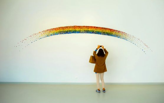 A woman stands observing a colorful rainbow art installation indoors.