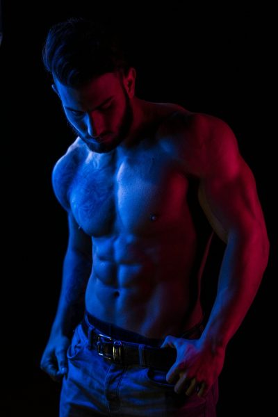Artistic photo of a shirtless muscular man in vibrant lighting, showcasing fitness and strength.